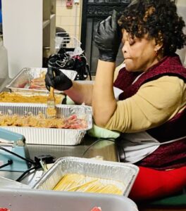 A lady in gloves preparing food in aluminum trays in a kitchen